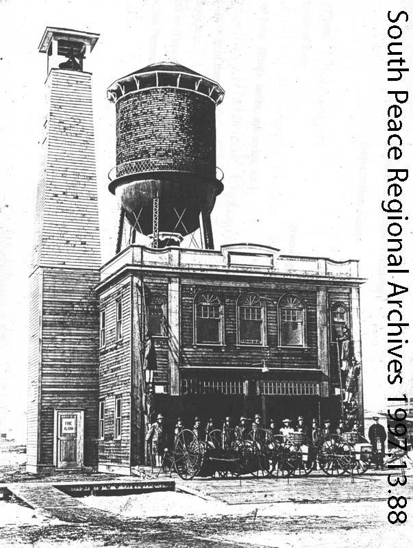 New fire hall and water tower with well-equipped firefighters ready for service, ca. 1920